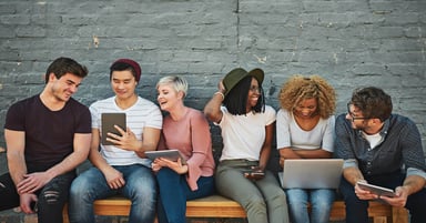 Young adults sitting on a bench laughing while looking at laptops