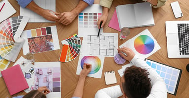 From the top shot of people looking at color grids on a table. 