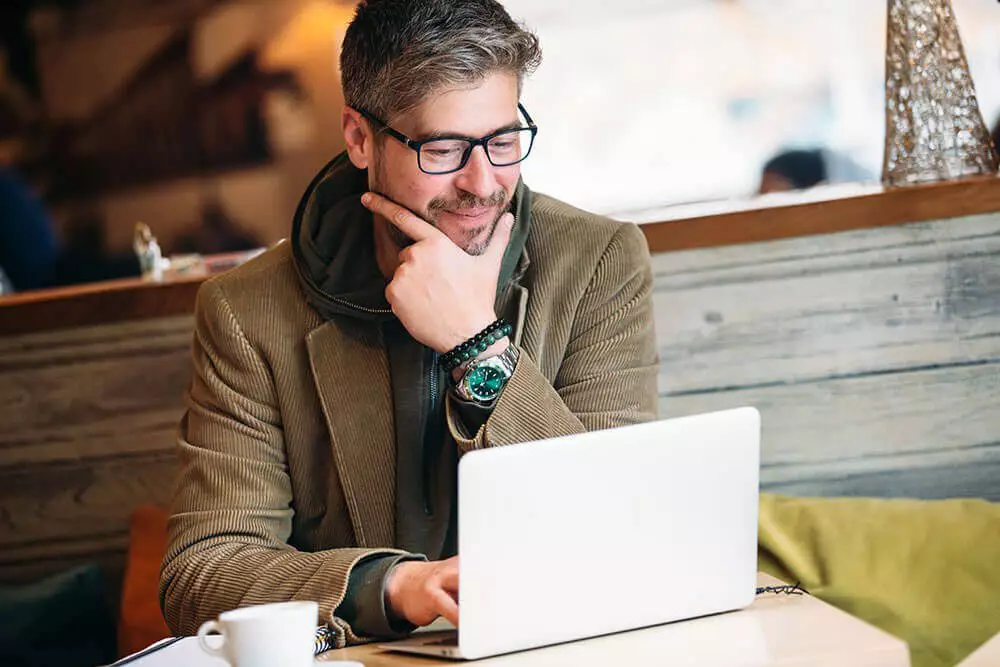 Man sitting on front of laptop in hand on face thinking.