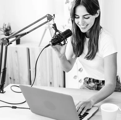 young woman sitting at table with laptop and microphone